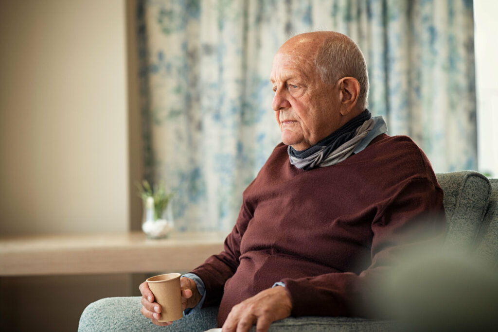 Sad elderly man sitting alone at home with a sad expression.