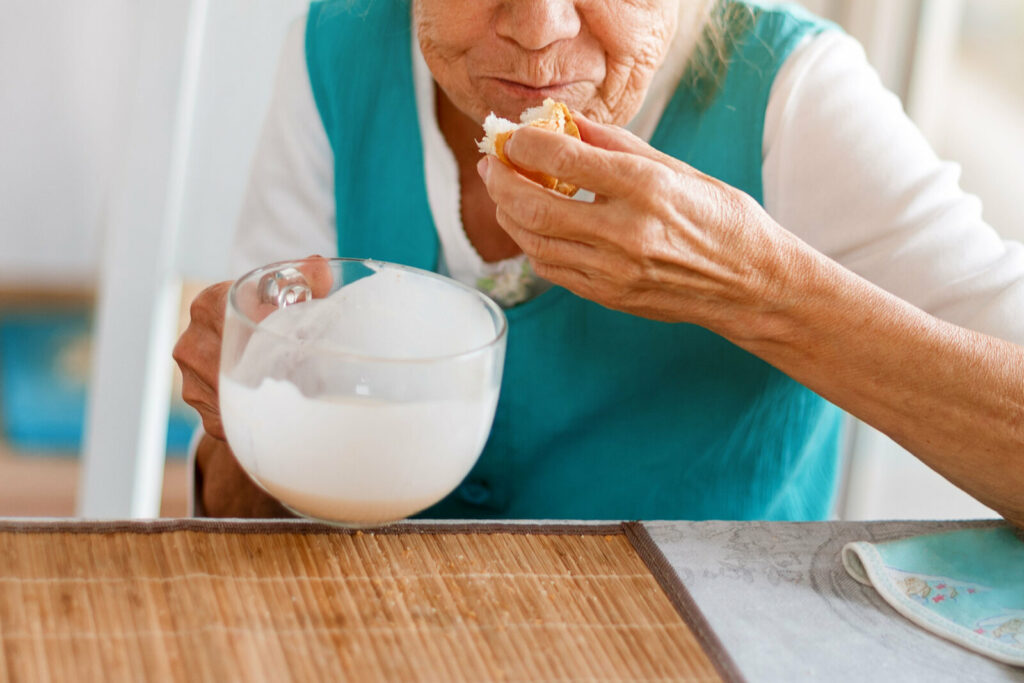 Senior woman hands holding big cup of yogurt and piece of brad.