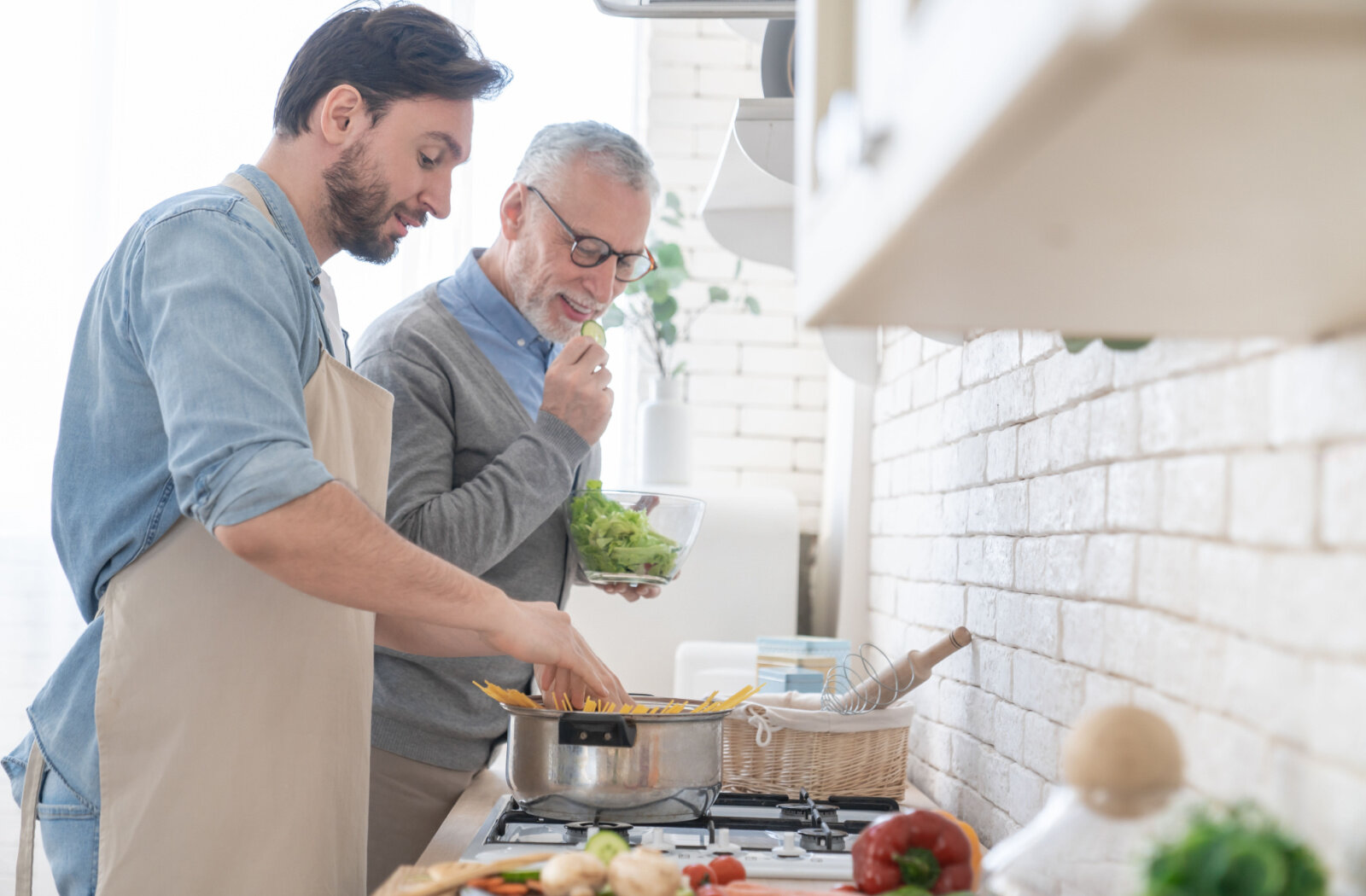 A young son helping his old senior father in preparing meal at home .