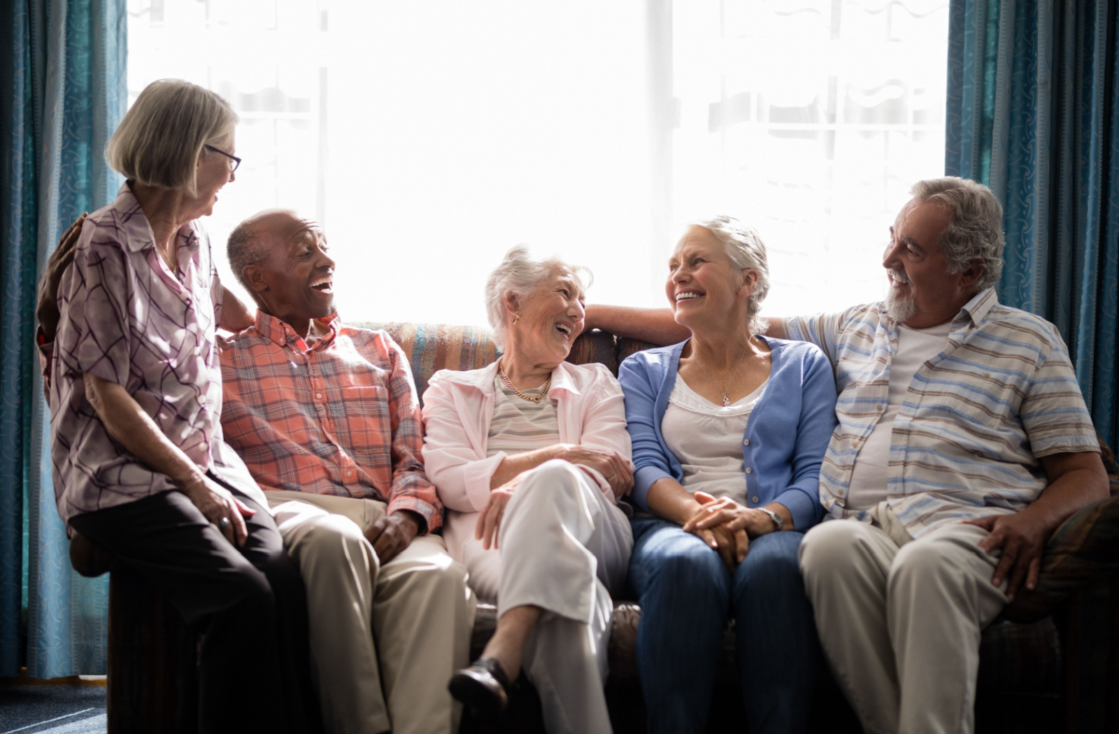 5 seniors sitting on a couch, smiling, and laughing.
