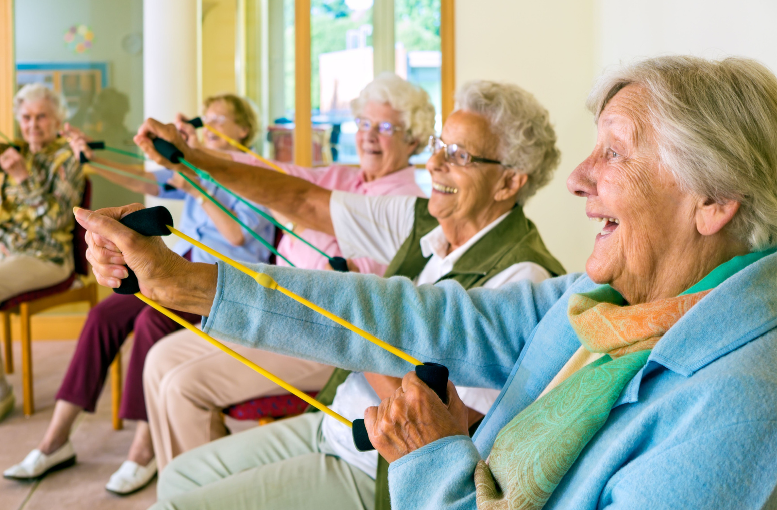 A group of senior women smiling while sitting on a circle and using exercise bands.