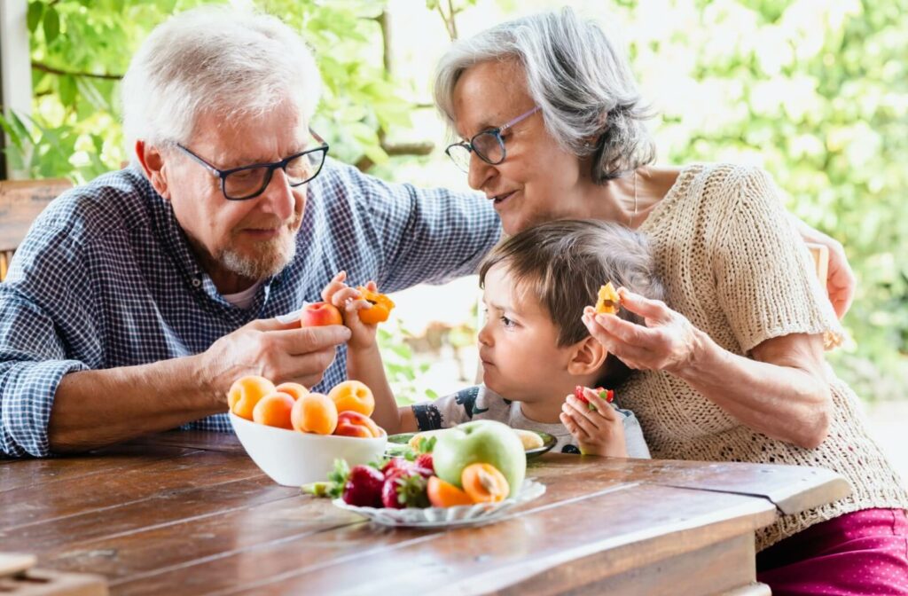 A pair of older adults eat healthy fruits & vegetables with their grandchild.