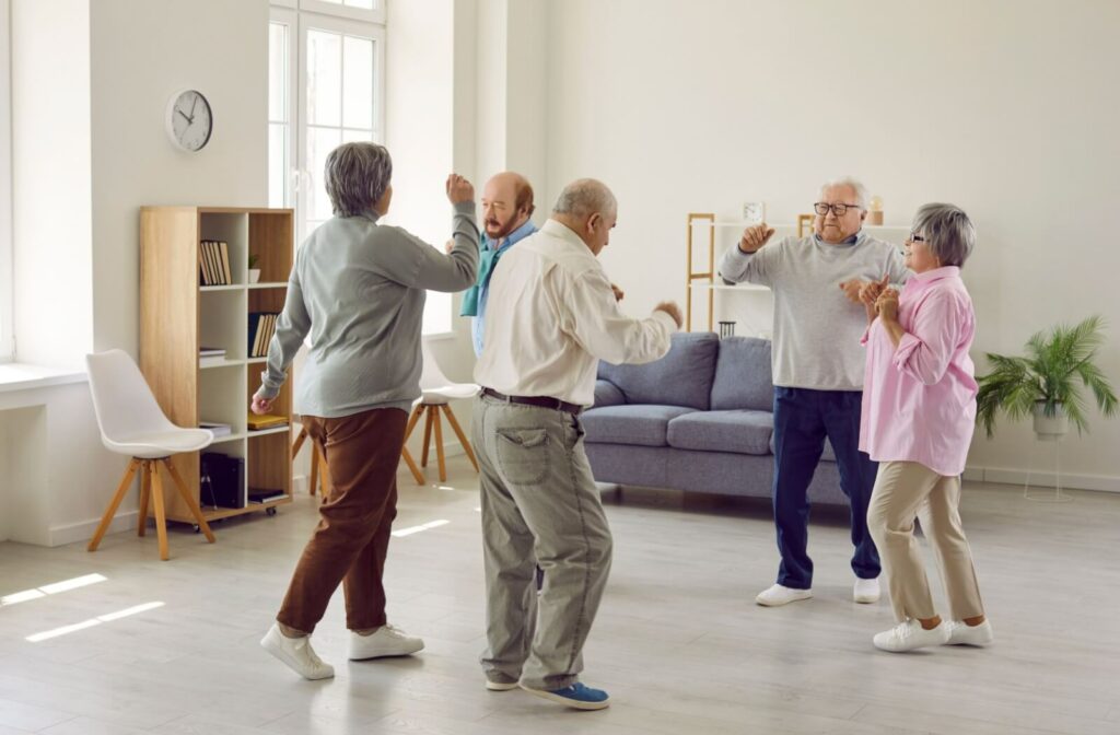 A happy and healthy group of elderly individuals dance in a dance class in a shared space in their assisted living home.