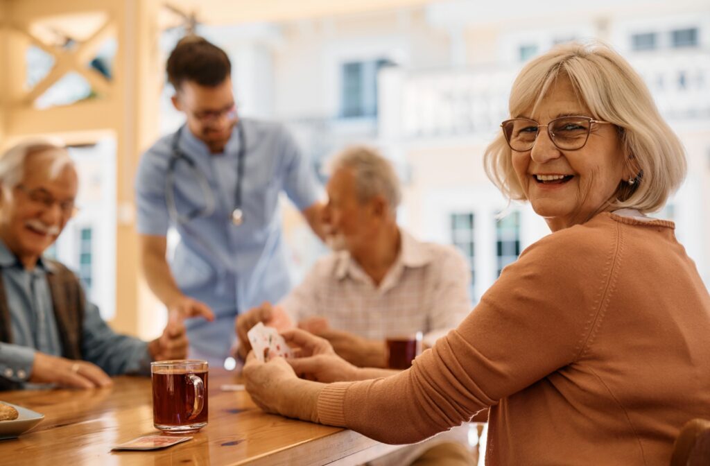 A senior woman smiling at the camera while sitting at an outdoor patio playing cards with her friends in senior living.