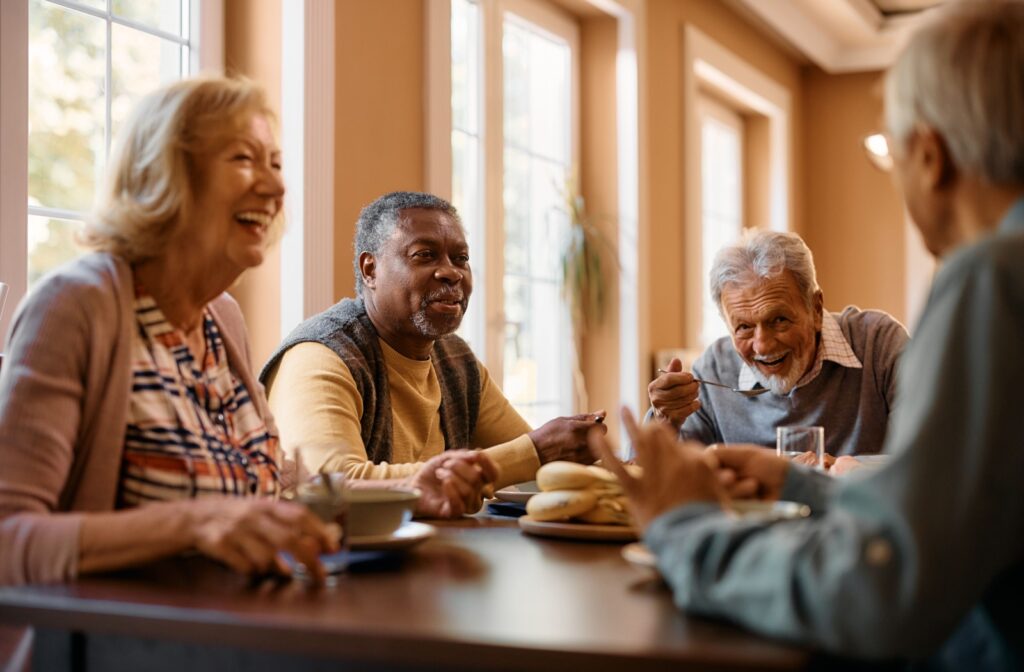 A group of seniors enjoying breakfast and laughing together in assisted living.