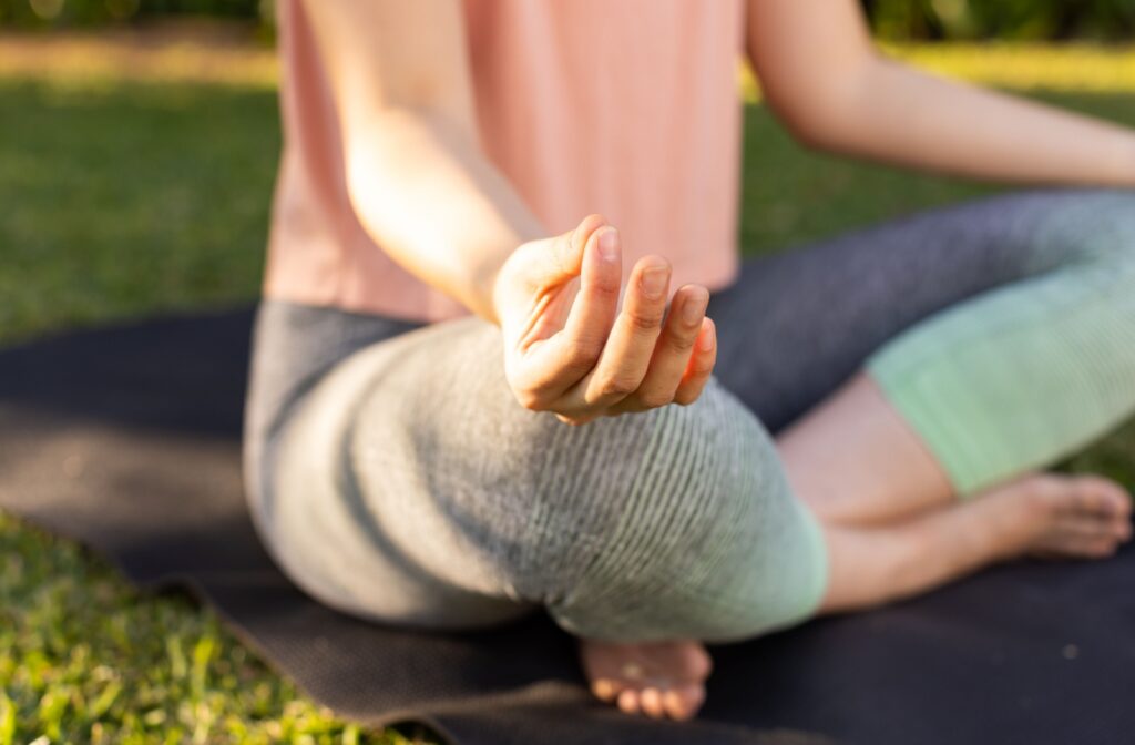 A cropped image shows a young woman engaging in mindful meditation on her yoga mat outside.