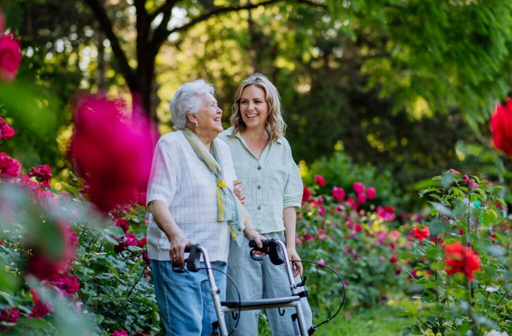 A daughter guides her older adult mom with a walker through a sensory garden.