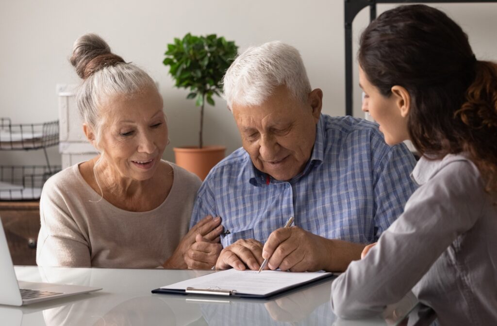 An elderly couple sitting with a young professional, reviewing and signing a document.