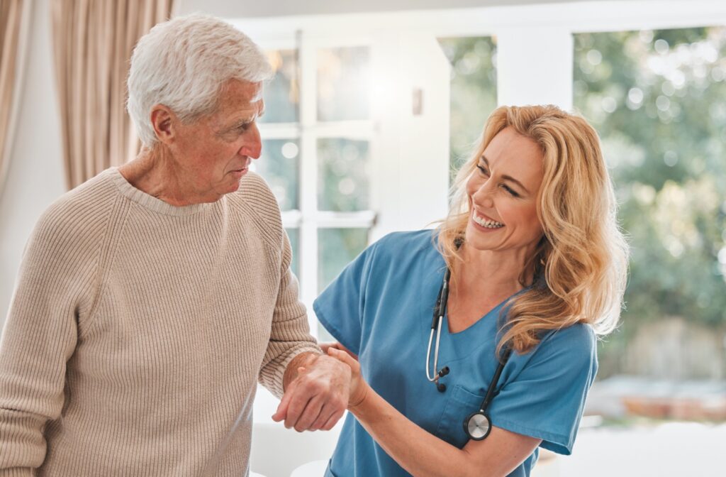 An assisted living staff member smiling and helping an older adult walk.