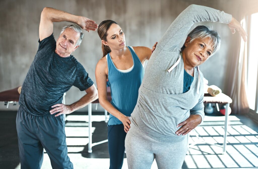 A physical therapist helps two seniors stretch and work on their sense of balance to support fall prevention