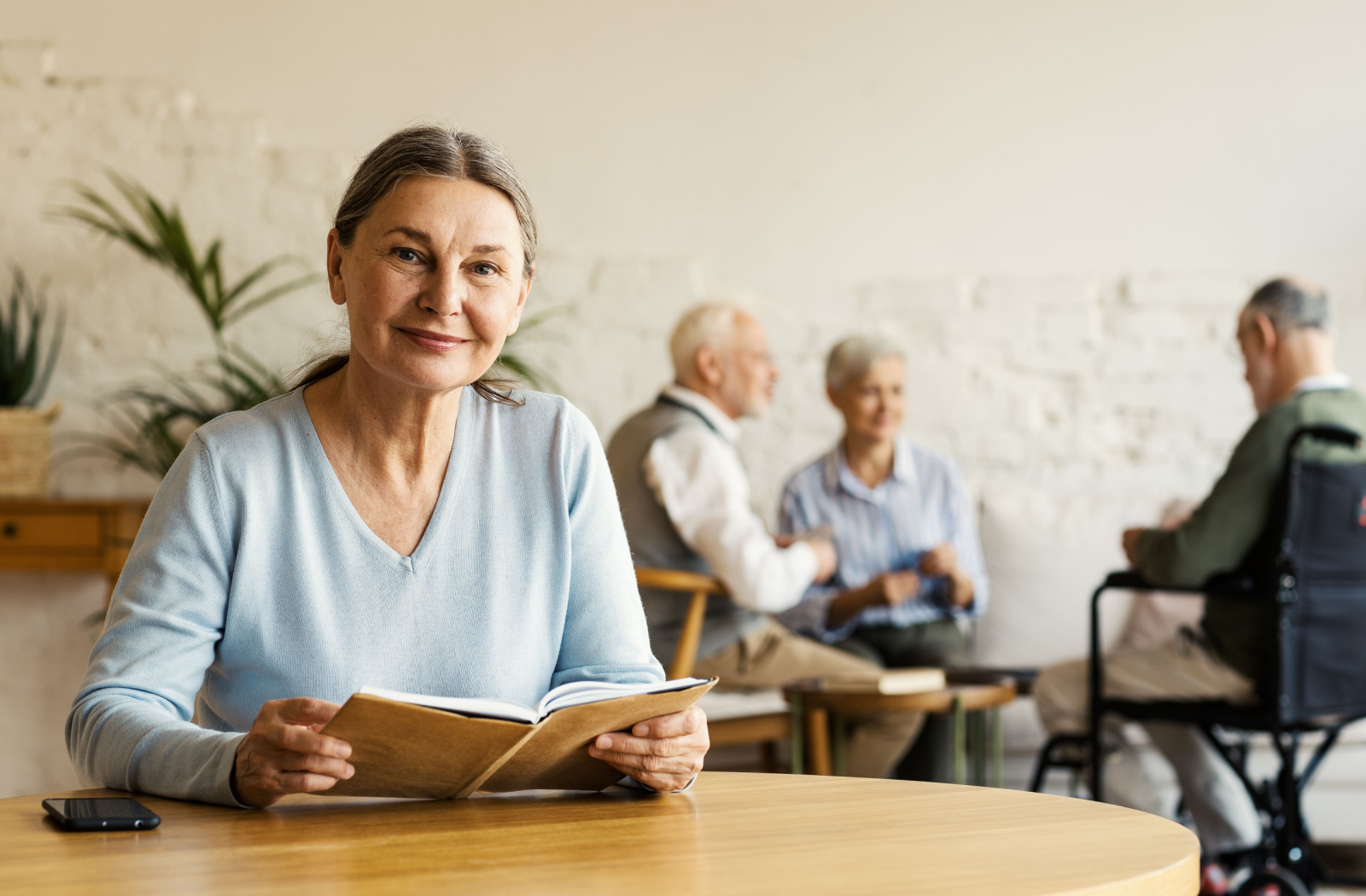 A senior woman with gray hair looking directly at the camera smiling and holding a book.