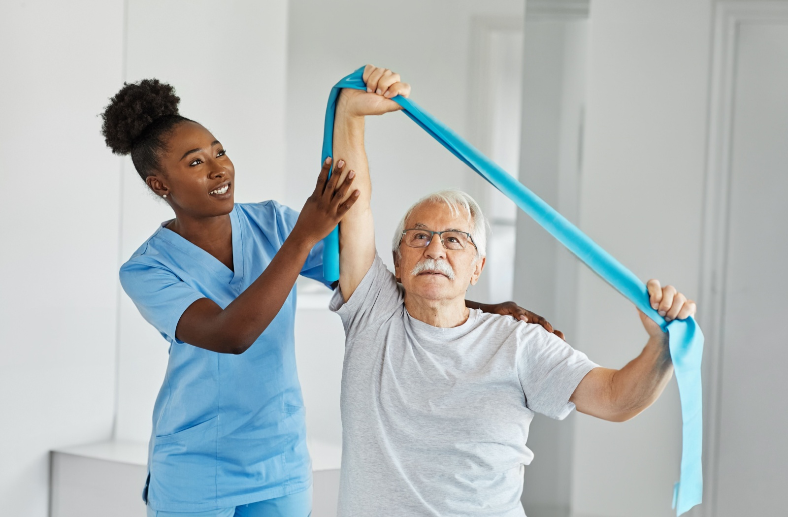 An older adult man practicing with an exercise band supervised by a nurse.