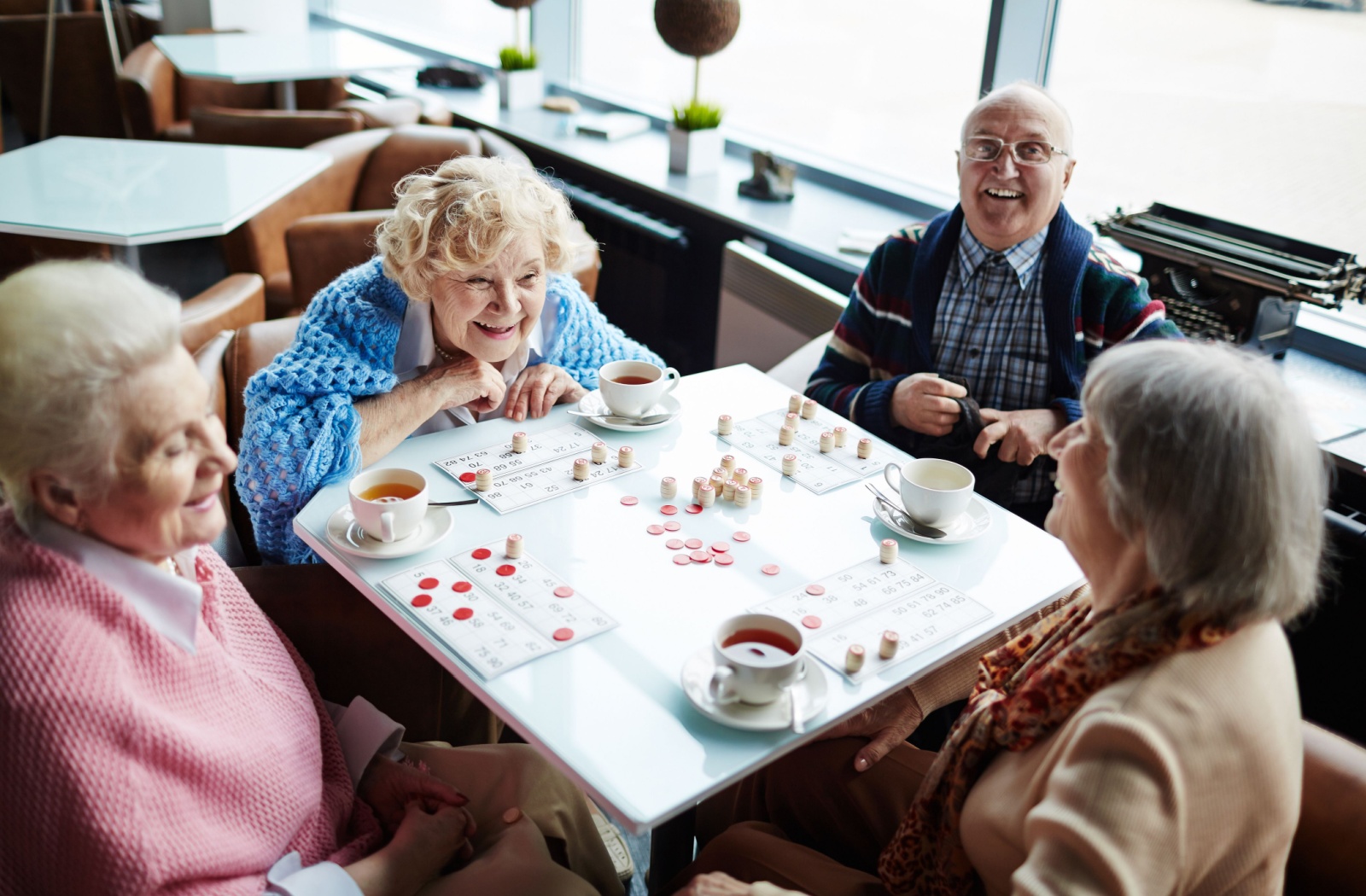Older adults gathered around a table playing a board game with tea.