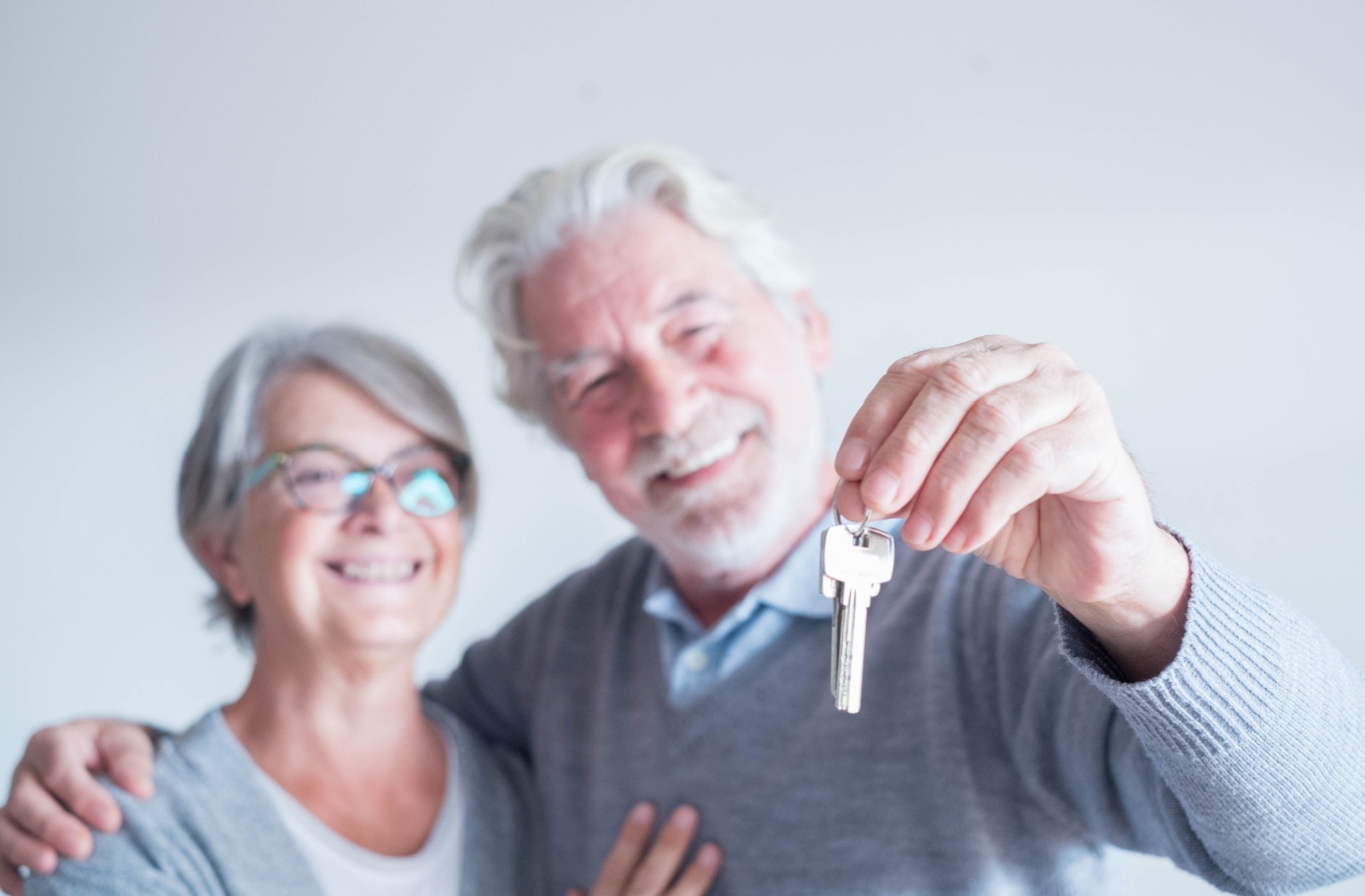A senior couple happily holds up the keys to their new room in their community.