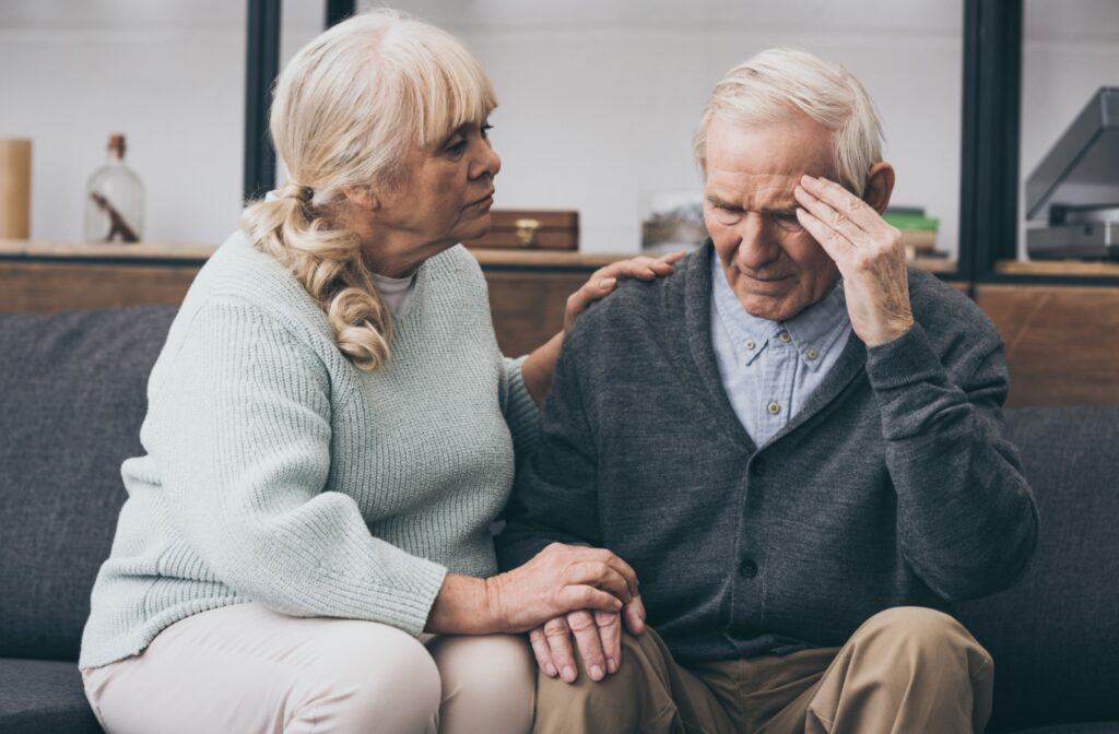 A senior attempts to comfort their partner as they hold a hand to their head, worried about progressing memory loss symptoms