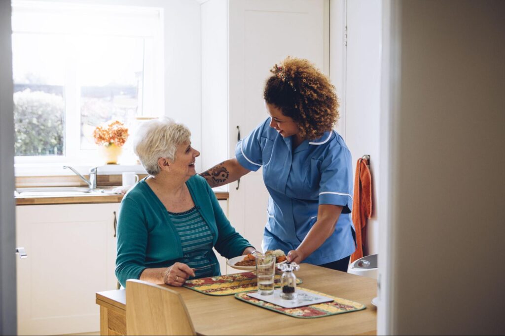 A senior living caregiver and older adult share a smile as the senior enjoys a delicious breakfast.