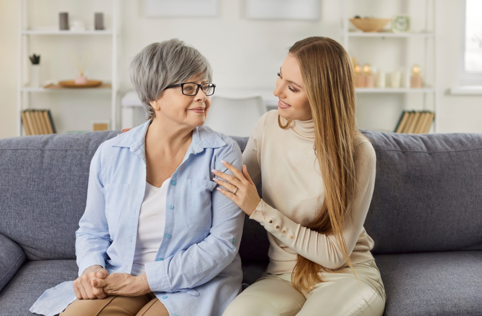 An adult child comforts their senior parent as they share a smile.