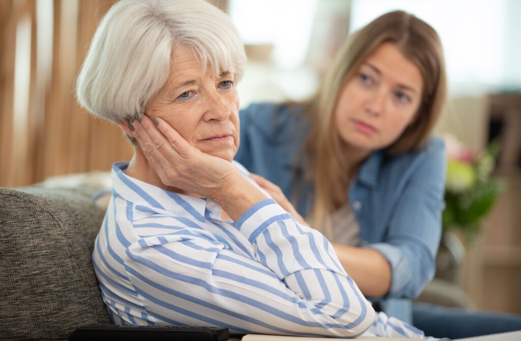 An adult child touches their parent's shoulder, showing worry, as their senior loved one looks away, expressing concern.