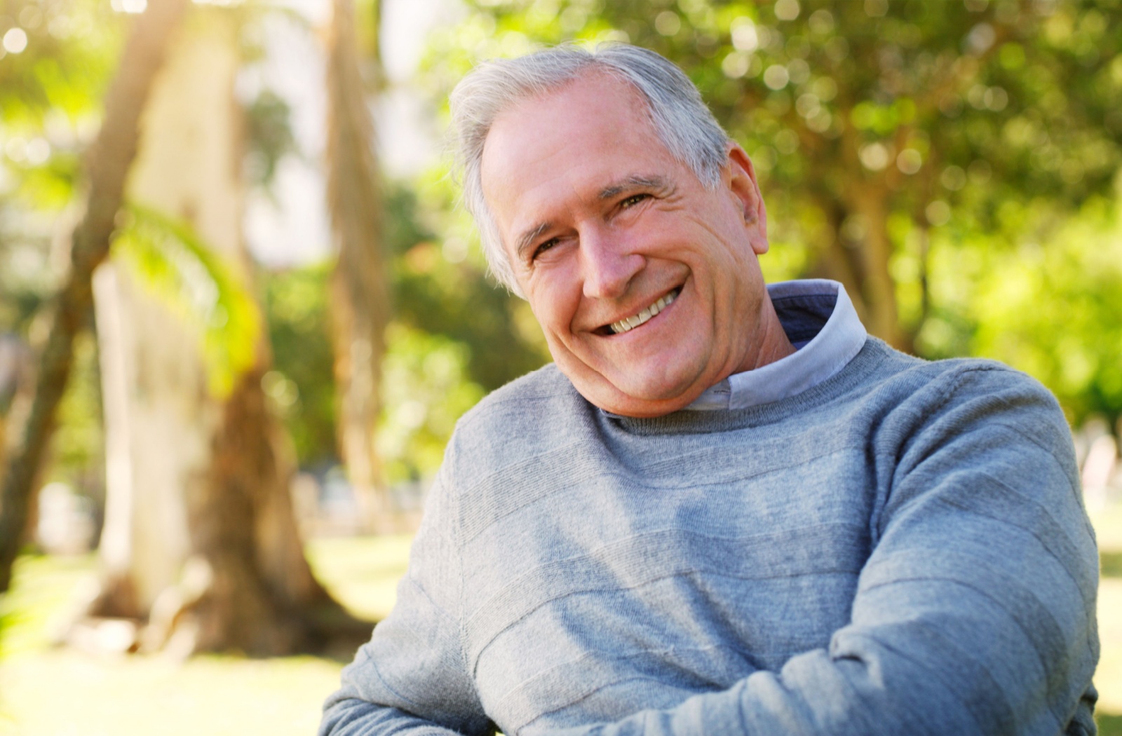 A senior sits outside and smiles at the camera, happy with their move into senior living.