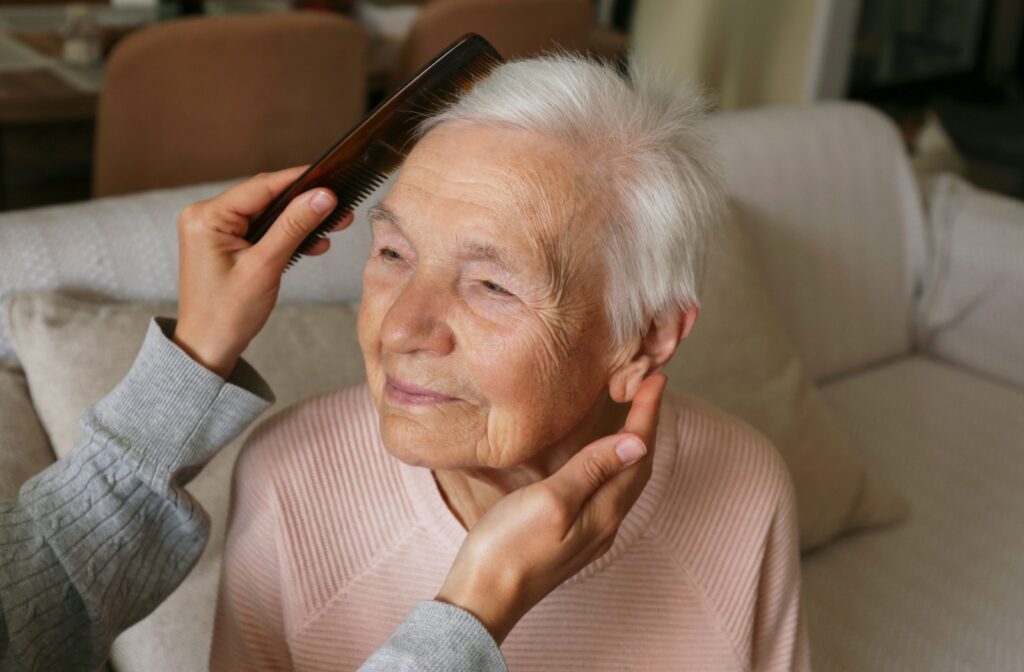 A senior in assisted living gets help with their hair in the morning.
